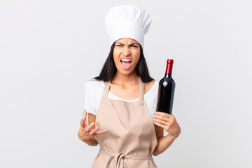 pretty hispanic chef woman looking angry, annoyed and frustrated and holding a bottle of wine