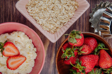 top view of cottage cheese   oatmeal flakes and fresh ripe strawberries in a wooden bowl on rustic background