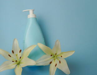 Creative still life makeup photo with blue cosmetic bottle with dispenser and fresh lily lights on blue background. View from above.