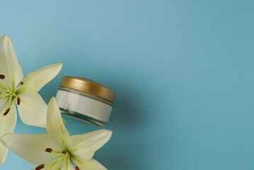 cosmetic jar of cream and yellow lily flower on blue boom