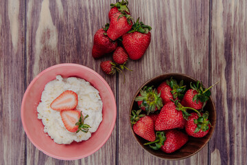 top view of cottage cheese in a pink bowl with fresh ripe strawberries on rustic wooden background