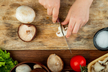 top view of female hands cutting fresh mushrooms on wooden cutting board and fresh tomatoes on wooden rustic background