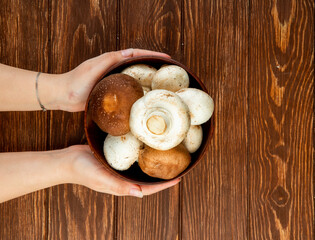 top view of female hands holding fresh mushrooms in a wooden bowl on rustic background