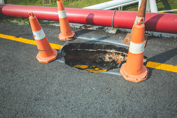 Deep sinkhole on a street city and orange traffic cone. Dangerous hole in the asphalt highway