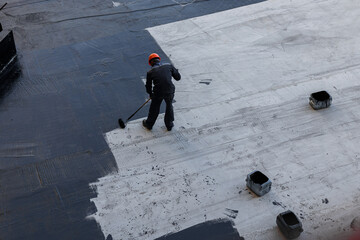 Waterproofing coating. A worker applies bitumen mastic to the foundation. Roofer cover the waterproofing primer on the roof, modified with polymer bitumen, with a roller brush. - obrazy, fototapety, plakaty