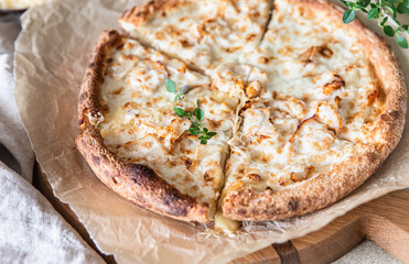 Homemade pizza with chicken and cheese on white sauce, light concrete background.