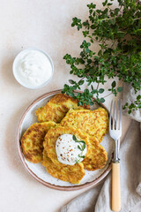 Vegetable fritters or pancakes with yoghurt or cream sour dressing and herbs. Cabbage or zucchini fritters on ceramic plate. Healthy vegetarian food. Top view.