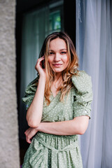 Fototapeta premium Young, slender girl in a dress in the morning stands in the balcony doorway