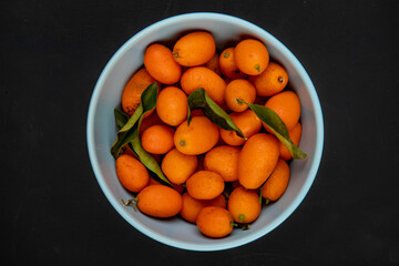 top view of fresh ripe kumquats in a blue bowl on black background