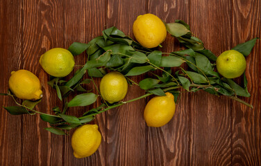 top view of fresh ripe lemons with green leaves on on rustic wooden background