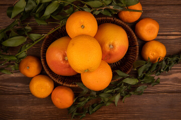 top view of fresh ripe oranges in a wicker basket and green leaves on dark wooden background