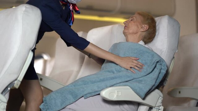 air hostess covering a blanket for senior woman passengers sleeping on plane.