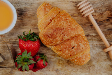 top view of fresh ripe strawberries with croissant and honey on a wooden background
