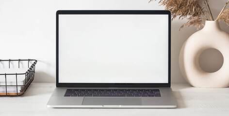 Home office desk with open laptop, storage basket, dry flowers in vase. Banner