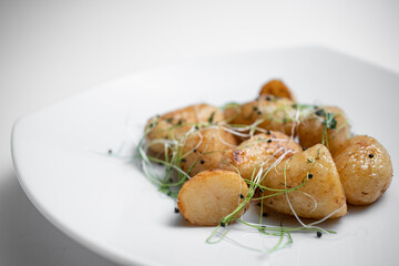 closeup of tasty roasted potatoes with microgreen on plate on white background