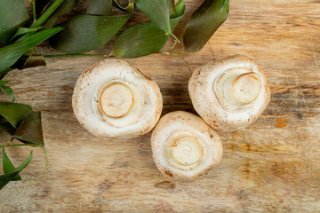 top view of fresh white mushrooms and green leaves on wooden background