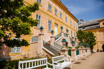 Fototapeta na wymiar Krasny Dvur Chateau, North Bohemia, Czech Republic, 19 June 2021: Baroque yellow castle with stairs, front yard with green lawn and white benches at sunny summer day