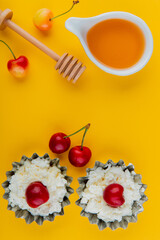 top view of honey with wooden spoon and cottage cheese in mini tart tins with fresh ripe rainier cherries on yellow background