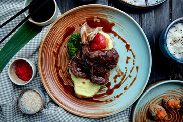 top view of mashed potatoes with roasted lamb chops and vegetables with soy sauce on a plate on wooden background