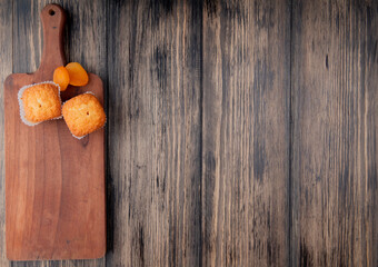 top view of muffins and dried apricots on wooden cutting board on rustic background with copy space