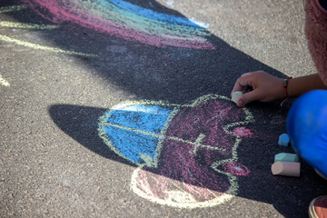 girl draws a rainbow, sun, car with chalk on the asphalt.