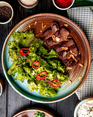 top view of roasted beef with lettuce and red chili pepper on a plate on wooden background