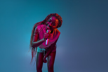Portrait of young charming african woman with microphone isolated over blue background in neon...