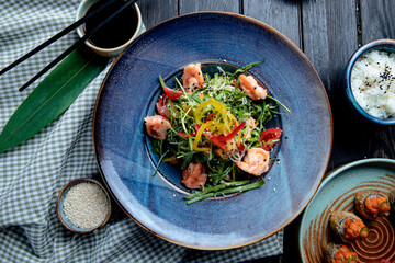 top view of shrimp salad with bell peppers and arugula on a plate on wooden background