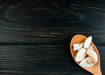 top view of sliced mushrooms in a wooden spoon on dark rustic background with copy space