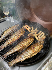 Delicious trout and german sausages are grilled together, process of cooking, healthy seafood.