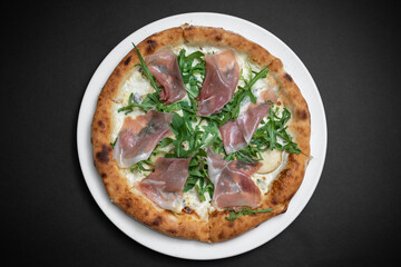 top view of pizza with prosciutto, arugula and cheese on black background