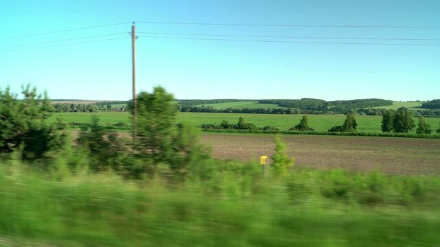 View from car window of green countryside fields and clear blue sky in summer sunny day. Trip, travel, journey by car. Transport, driving on road.