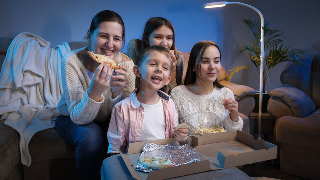 Happy Family Smiling And Laughing While Eating Pizza And Watching TV Movie Or Show At Night.