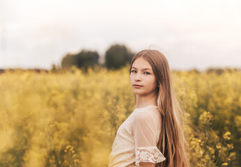 Portrait of a beautiful young girl with long hair against the background of rapeseed flowers. Youth and nature