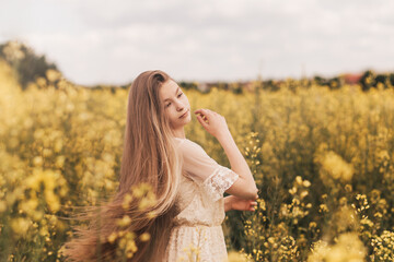 Fototapeta na wymiar Portrait of a beautiful young girl with long hair against the background of rapeseed flowers. Youth and nature