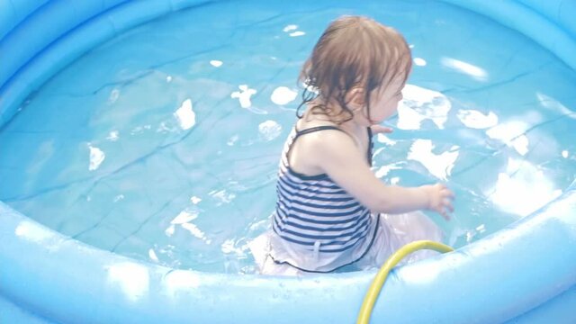 A little girl in an inflatable pool. Backyard of the house, outdoor, rest in nature. Happiness, joy, smile, funny children. Water, an active lifestyle. two-year-old girl looks into the camera