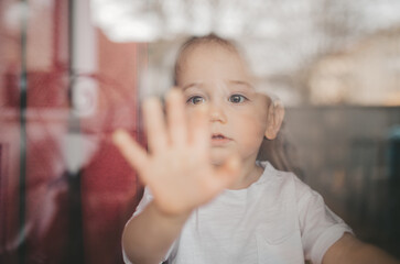 A young boy is inside the house and has hand Against Window Glass.