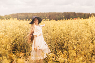 Fototapeta na wymiar A young happy girl enjoys nature on the field of blossoming canola. The corcept of youth and freedom.