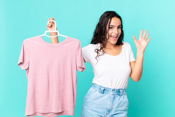 hispanic pretty woman smiling happily, waving hand, welcoming and greeting you choosing a cloth