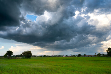 Dark sky and dramatic black cloud before rain.rainy storm over rice fields with rural road,Sisaket province,Thailand.