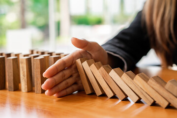 A businesswoman blocks a falling wooden block like a domino. It is like stopping business risks with a strategy. and project management the best of the business