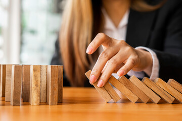 A businesswoman blocks a falling wooden block like a domino. It is like stopping business risks with a strategy. and project management the best of the business