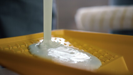 Unknown person filling yellow container with white paint in new apartment.