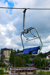 Empty bench of ski lift on a mountain in blue on a blurred background from buildings of a tourist resort in summer