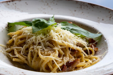 spaghetti carbonara in a white plate on the table in a restaurant. Durum wheat pasta with bacon, cheese and cream sauce.