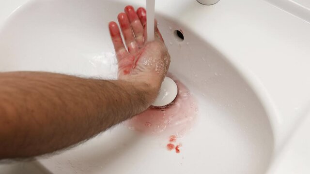 A murderer or serial killer washing his bloody hand in the bathroom sink.