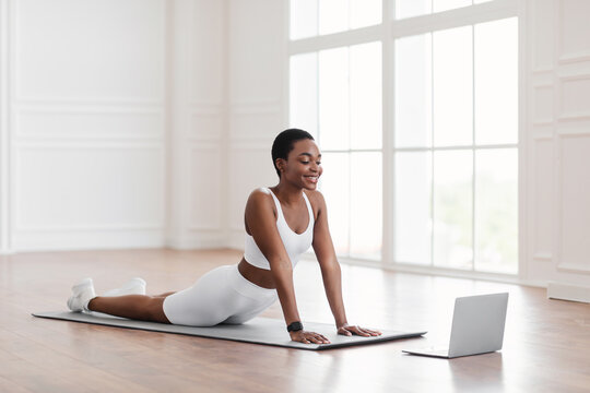Young african woman stretching back on mat with pc