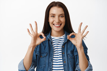 No problem, yes its alright. Smiling young woman looks satisfied, shows okay zero OK gesture, nod...