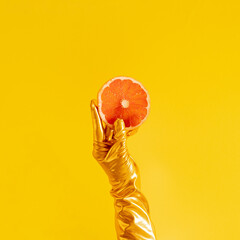 hand with a golden glove and slice of fresh grapefruit on yellow sunny summer illuminating...