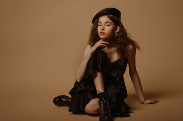 Fashion conception:  confident curly brunette woman wearing total black outfit with beret, dress with ruffles, lace up chunky sole ankle leather  boots. Full body studio portrait. Copy, empty space 